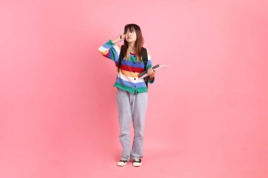 Renkli gökkuşağı kıyafetleri giyen Asyalı kadın ya da okul çantası ve kitap taşırken gündelik görünüş pembe arka planda izole edilmiş bir düşünce jesti. Gen Z