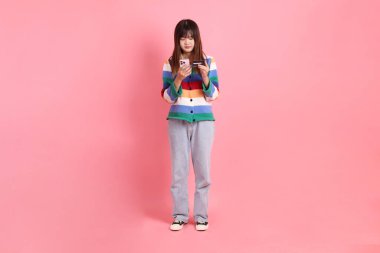 Renkli gökkuşağı kıyafetleri giyen Asyalı bir kadın ya da pembe arka planda cep telefonu olan kredi kartı tutan sıradan görünüşlü bir kadın. Gen Z