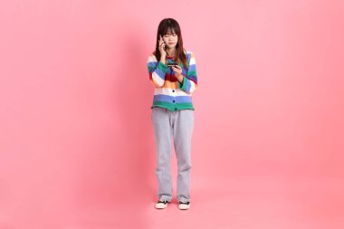 Renkli gökkuşağı kıyafetleri giyen Asyalı bir kadın ya da pembe arka planda cep telefonu olan kredi kartı tutan sıradan görünüşlü bir kadın. Gen Z