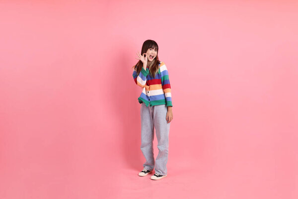 Азиатская женщина носит красочные радужные зимние одежды или случайный взгляд с жестом больших пальцев вверх, хорошо или подтвердить изолированы на розовом фоне. Gen Z
