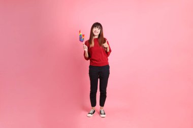 Kırmızı günlük tişörtlü genç Asyalı kadın başparmak kaldırırken Onur Bayraklarını Tutma jesti, pembe arka planda izole edilmiş. Gen Z