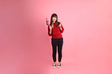 Genç Asyalı kadın, pembe arka planda izole edilmiş, kalp şeklinde küçük bir kalp yaparken Onur Bayraklarını Tutma jesti ile kırmızı günlük tişörtlü. Gen Z