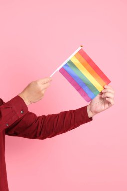 İki elinde de pembe arka planda izole edilmiş Rainbown Pride Bayrakları olan resmi ve sıradan kırmızı tişörtlü Asyalı kıdemli bir adam. LGBTQ + topluluğu