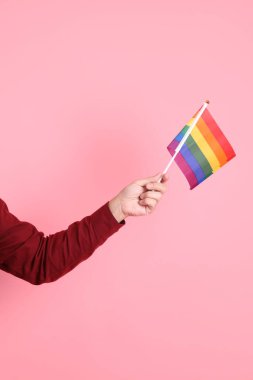 İki elinde de pembe arka planda izole edilmiş Rainbown Pride Bayrakları olan resmi ve sıradan kırmızı tişörtlü Asyalı kıdemli bir adam. LGBTQ + topluluğu