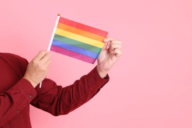 İki elinde de pembe arka planda izole edilmiş Rainbown Pride Bayrakları olan resmi ve sıradan kırmızı tişörtlü Asyalı kıdemli bir adam. LGBTQ + topluluğu