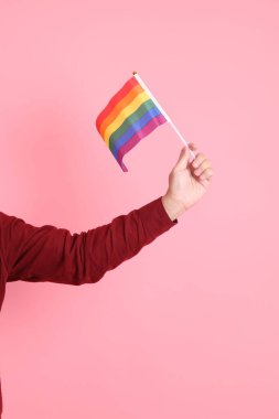 İki elinde de pembe arka planda izole edilmiş Rainbown Pride Bayrakları olan resmi ve sıradan kırmızı tişörtlü Asyalı kıdemli bir adam. LGBTQ + topluluğu