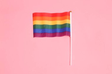 İki elinde de pembe arka planda izole edilmiş Rainbown Pride Bayrakları olan resmi ve sıradan kırmızı tişörtlü Asyalı kıdemli bir adam. LGBTQ + topluluğu