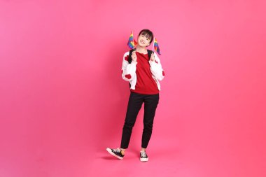 Kırmızı tişörtlü Asyalı bir kadın ya da günlük kıyafetler, kırmızı kalp şeklinde gömlek ve pembe arka planda tutulan Onur Bayrakları jesti. Gen Z LGBTQ + topluluğu