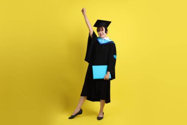 Mavi mezuniyet elbiseleri ve kepleri içinde, elinde diplomaları olan, heyecanlı, sarı arka planda izole bir şekilde kutlanan bir üniversite öğrencisi. Gen Z, yeni mezun, eğitim, ilk iş