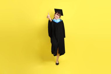 Mavi mezuniyet elbisesi ve şapkalı bayan üniversite öğrencisi, tamam ya da sarı arka planda izole edilmiş. Gen Z, yeni mezun, eğitim, ilk iş