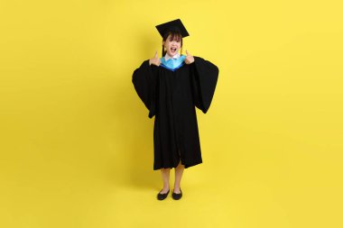 Mavi mezuniyet elbisesi ve şapkalı bayan üniversite öğrencisi, tamam ya da sarı arka planda izole edilmiş. Gen Z, yeni mezun, eğitim, ilk iş