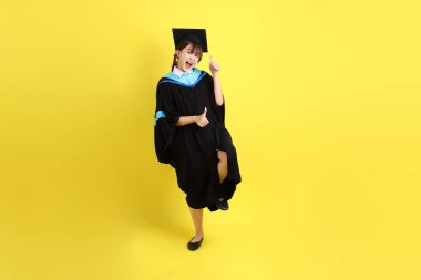 Mavi mezuniyet elbisesi ve şapkalı bayan üniversite öğrencisi, tamam ya da sarı arka planda izole edilmiş. Gen Z, yeni mezun, eğitim, ilk iş