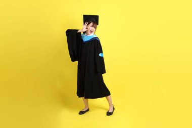 Mavi mezuniyet elbisesi ve şapkalı bayan üniversite öğrencisi, tamam ya da sarı arka planda izole edilmiş. Gen Z, yeni mezun, eğitim, ilk iş