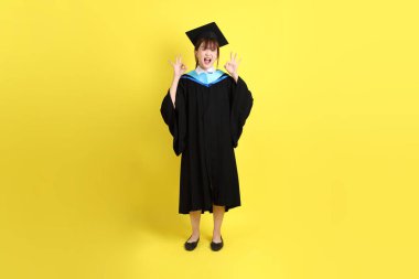 Mavi mezuniyet elbisesi ve şapkalı bayan üniversite öğrencisi, tamam ya da sarı arka planda izole edilmiş. Gen Z, yeni mezun, eğitim, ilk iş