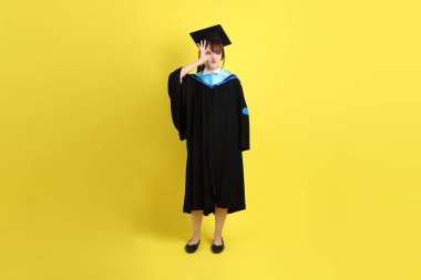 Mavi mezuniyet elbisesi ve şapkalı bayan üniversite öğrencisi, tamam ya da sarı arka planda izole edilmiş. Gen Z, yeni mezun, eğitim, ilk iş