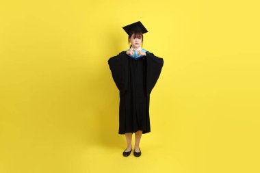 Mavi mezuniyet elbisesi ve şapkalı, sarı arka planda izole edilmiş, durdurulmuş, yasaklanmış ve reddedilmiş bir üniversite öğrencisi. Gen Z, yeni mezun, eğitim, ilk iş