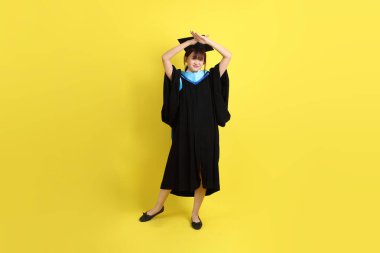 Mavi mezuniyet elbisesi ve şapkalı, sarı arka planda izole edilmiş, durdurulmuş, yasaklanmış ve reddedilmiş bir üniversite öğrencisi. Gen Z, yeni mezun, eğitim, ilk iş