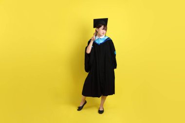 Mavi mezuniyet elbisesi ve şapkalı, sarı arka planda izole edilmiş, durdurulmuş, yasaklanmış ve reddedilmiş bir üniversite öğrencisi. Gen Z, yeni mezun, eğitim, ilk iş