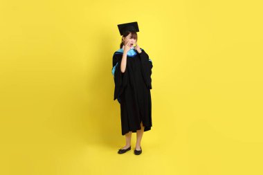 Mavi mezuniyet elbisesi ve kepleri içinde, sarı arka planda izole edilmiş, verme ve alma hareketi yapan bir üniversite öğrencisi. Gen Z, yeni mezun, eğitim, ilk iş