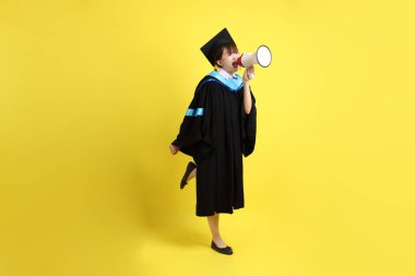 Mavi mezuniyet elbiseleri ve kepleri içinde elinde megafonla sarı arka plan izole bir şekilde bağıran bir üniversite öğrencisi. Gen Z, yeni mezun, eğitim, ilk iş