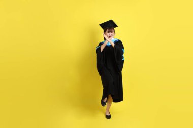 Mavi mezuniyet elbisesi ve şapkalı, sarı arka planda izole edilmiş, durdurulmuş, yasaklanmış ve reddedilmiş bir üniversite öğrencisi. Gen Z, yeni mezun, eğitim, ilk iş