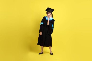 Sarı arka planda diş ağrısı jesti olan mavi mezuniyet elbisesi ve şapkalı bir üniversite öğrencisi. Gen Z, yeni mezun, eğitim, ilk iş