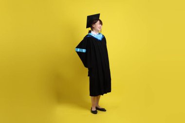 Sarı arka planda sırtı ağrıyan mavi önlüklü ve kepli bir üniversite öğrencisi. Gen Z, yeni mezun, eğitim, ilk iş