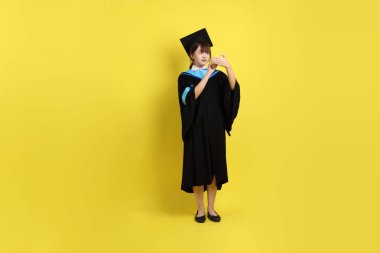 Mavi mezuniyet elbisesi ve şapkalı, not alma hareketi ve sarı arka planda izole edilmiş kısa notla bir üniversite öğrencisi. Gen Z, yeni mezun, eğitim, ilk iş