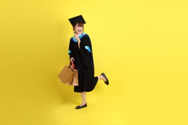 Sarı arka planda, mavi mezuniyet elbiseleri ve kepleri olan, alışveriş çantası taşıyan bir üniversite öğrencisi. Gen Z, yeni mezun, eğitim, ilk iş