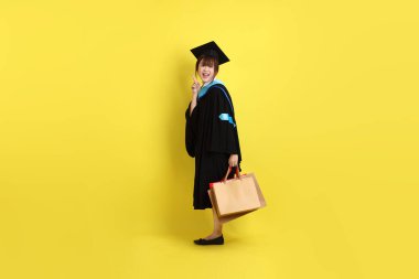 Sarı arka planda, mavi mezuniyet elbiseleri ve kepleri olan, alışveriş çantası taşıyan bir üniversite öğrencisi. Gen Z, yeni mezun, eğitim, ilk iş