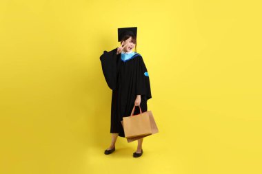 Sarı arka planda, mavi mezuniyet elbiseleri ve kepleri olan, alışveriş çantası taşıyan bir üniversite öğrencisi. Gen Z, yeni mezun, eğitim, ilk iş