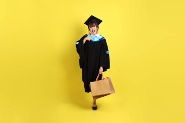 Sarı arka planda, mavi mezuniyet elbiseleri ve kepleri olan, alışveriş çantası taşıyan bir üniversite öğrencisi. Gen Z, yeni mezun, eğitim, ilk iş