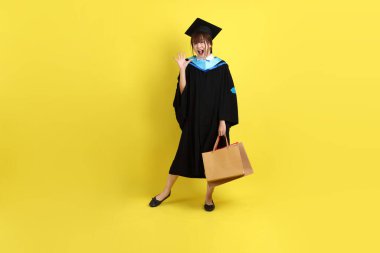 Sarı arka planda, mavi mezuniyet elbiseleri ve kepleri olan, alışveriş çantası taşıyan bir üniversite öğrencisi. Gen Z, yeni mezun, eğitim, ilk iş