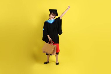 Sarı arka planda, mavi mezuniyet elbiseleri ve kepleri olan, alışveriş çantası taşıyan bir üniversite öğrencisi. Gen Z, yeni mezun, eğitim, ilk iş