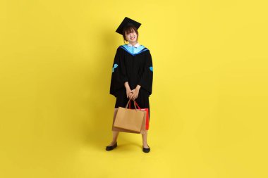 Sarı arka planda, mavi mezuniyet elbiseleri ve kepleri olan, alışveriş çantası taşıyan bir üniversite öğrencisi. Gen Z, yeni mezun, eğitim, ilk iş