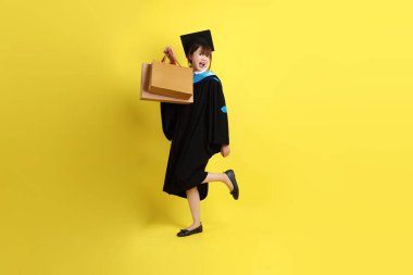 Sarı arka planda, mavi mezuniyet elbiseleri ve kepleri olan, alışveriş çantası taşıyan bir üniversite öğrencisi. Gen Z, yeni mezun, eğitim, ilk iş