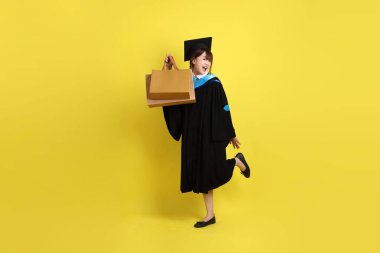 Sarı arka planda, mavi mezuniyet elbiseleri ve kepleri olan, alışveriş çantası taşıyan bir üniversite öğrencisi. Gen Z, yeni mezun, eğitim, ilk iş