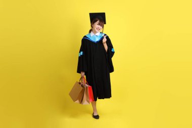 Sarı arka planda, mavi mezuniyet elbiseleri ve kepleri olan, alışveriş çantası taşıyan bir üniversite öğrencisi. Gen Z, yeni mezun, eğitim, ilk iş