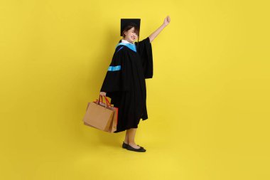 Sarı arka planda, mavi mezuniyet elbiseleri ve kepleri olan, alışveriş çantası taşıyan bir üniversite öğrencisi. Gen Z, yeni mezun, eğitim, ilk iş