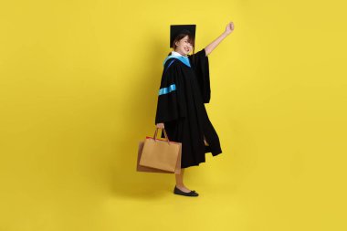 Sarı arka planda, mavi mezuniyet elbiseleri ve kepleri olan, alışveriş çantası taşıyan bir üniversite öğrencisi. Gen Z, yeni mezun, eğitim, ilk iş