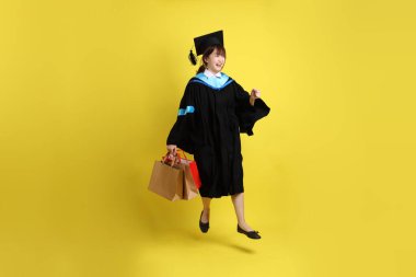 Sarı arka planda, mavi mezuniyet elbiseleri ve kepleri olan, alışveriş çantası taşıyan bir üniversite öğrencisi. Gen Z, yeni mezun, eğitim, ilk iş