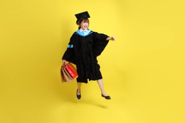 Sarı arka planda, mavi mezuniyet elbiseleri ve kepleri olan, alışveriş çantası taşıyan bir üniversite öğrencisi. Gen Z, yeni mezun, eğitim, ilk iş