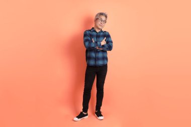 Yeşil ekose giysili, gözlüklü, kolları çapraz ve turuncu arka planda tek başına duran Asyalı son sınıf öğrencisi. Turist, akıllı gündelik.