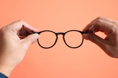 Yeşil ekose elbiseli Asyalı son sınıf öğrencisi. Turuncu arka planda gözlük tutan el hareketleriyle. Turist, akıllı gündelik.