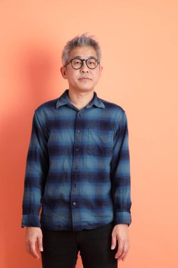 Yeşil ekose giysili Asyalı son sınıf öğrencisi gözlüklü, ayakta duran ve turuncu arka planda sırıtan. Turist, akıllı gündelik.