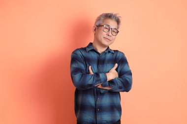 Yeşil ekose giysili, gözlüklü, kolları çapraz ve turuncu arka planda tek başına duran Asyalı son sınıf öğrencisi. Turist, akıllı gündelik.