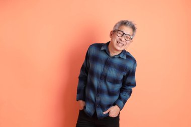 Yeşil ekose giysili Asyalı son sınıf öğrencisi gözlüklü, ayakta duran ve turuncu arka planda sırıtan. Turist, akıllı gündelik.