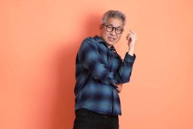 Yeşil ekose giysili Asyalı son sınıf öğrencisi gözlüklü, ayakta duran ve turuncu arka planda sırıtan. Turist, akıllı gündelik.