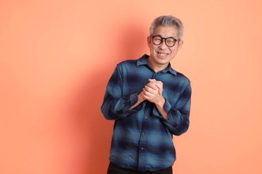 Yeşil ekose giysili Asyalı son sınıf öğrencisi gözlüklü, ayakta duran ve turuncu arka planda sırıtan. Turist, akıllı gündelik.