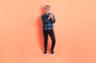 Yeşil ekose giysili Asyalı son sınıf öğrencisi gözlüklü, ayakta duran ve turuncu arka planda sırıtan. Turist, akıllı gündelik.